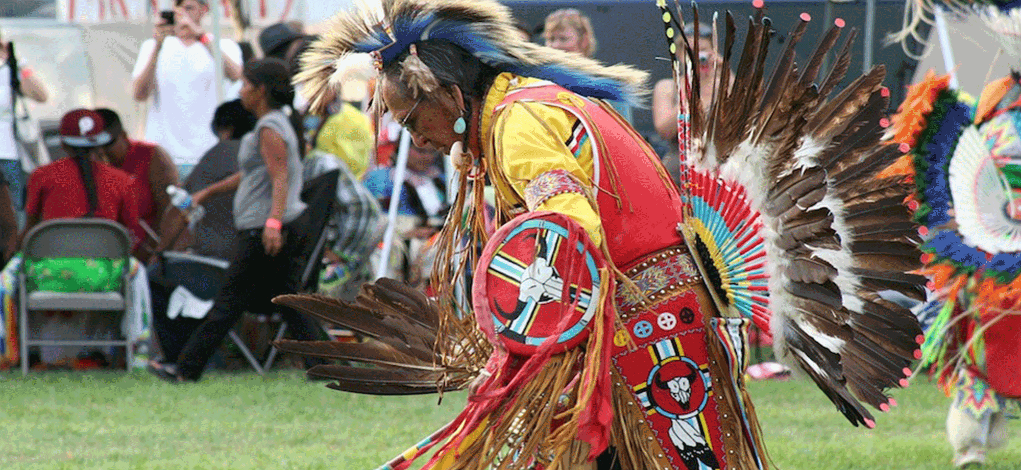 Photograph of a First Nations man in ceremonial dress dancing at a gathering